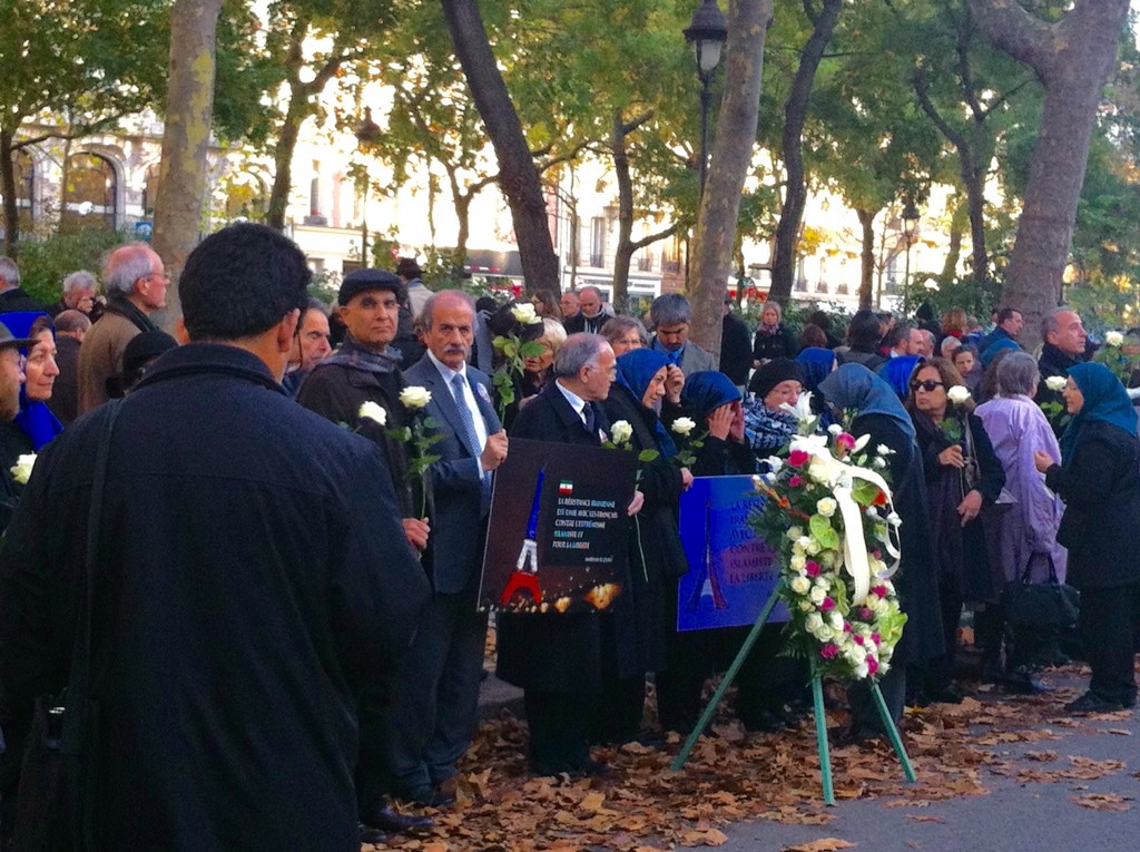 Across from the Bataclan, a group of protesters hold white roses and a sign that identifies them as the Iranian resistance, in unity with France.